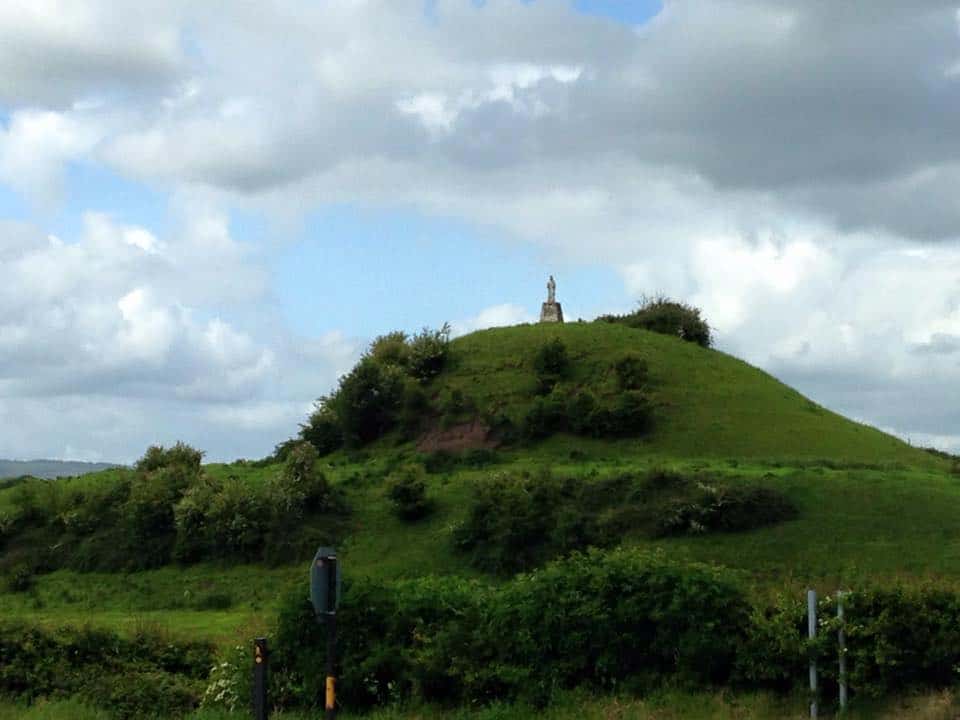 The Long Walk North – Day 12 Vibrant green hill with a statue at the top, under a partly cloudy sky, ideal for hiking and outdoor adventures.
