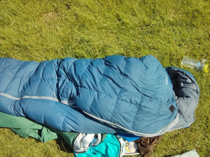 Getting a good night’s sleep on the trail Warm blue sleeping bag laid out on green grass for hiking or camping trips.
