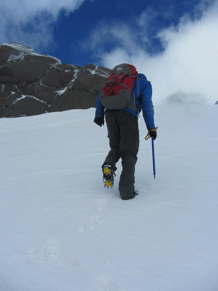 Ice axes ahoy Climber ascending snowy mountain terrain with backpack and trekking poles in cold weather adventure scene.