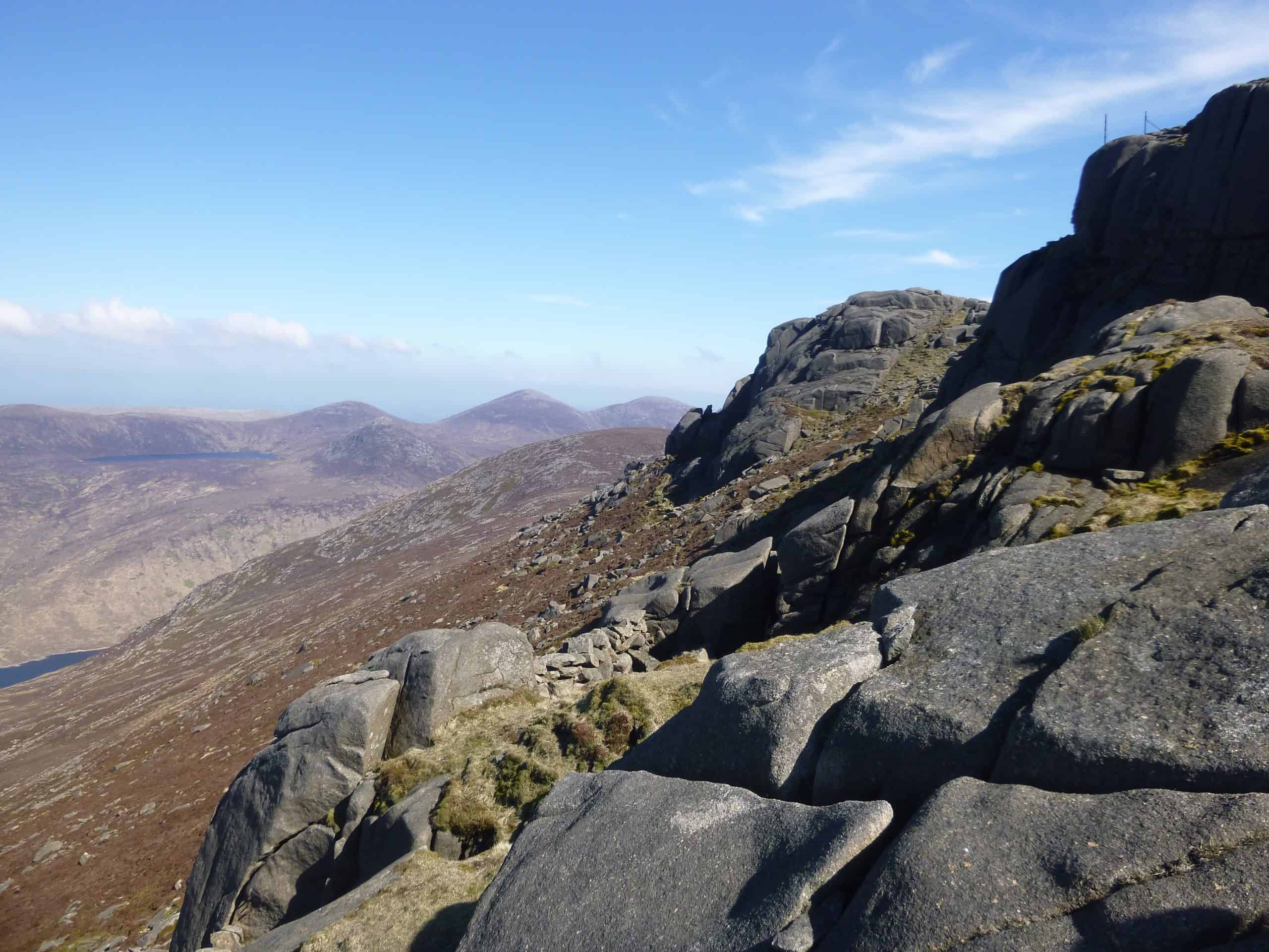 Rough stone wall on a mountain trail at dusk with dark sky and shadowed landscape, outdoor hiking scenery, rugged trail, natural landscape, adventure hiking, scenic mountain path, wilderness exploration, remote outdoor environment.