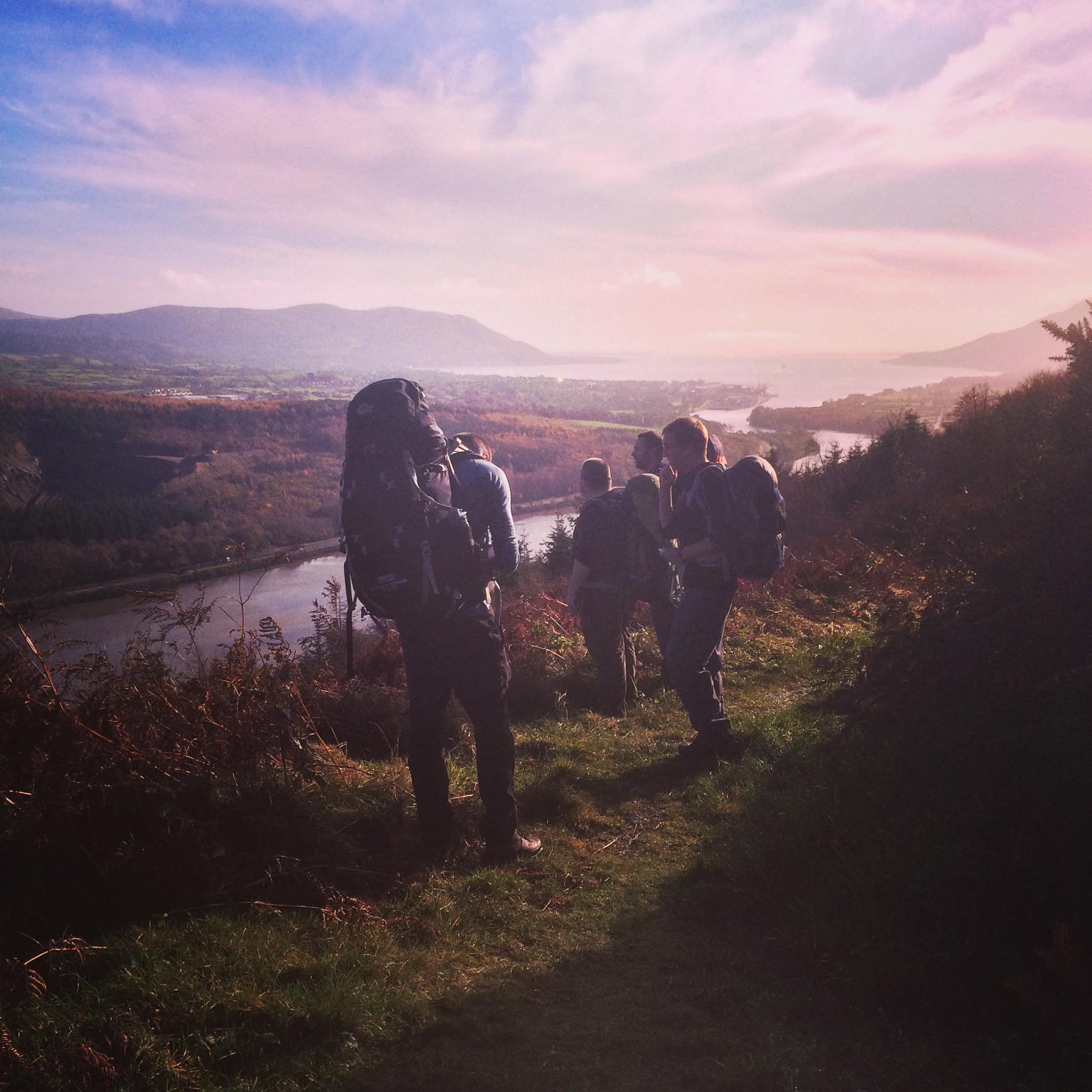 The Ring of Gullion Way Hikers enjoying scenic views during a day hike in nature with backpacks and hiking gear on a trail overlooking a river and mountains.
