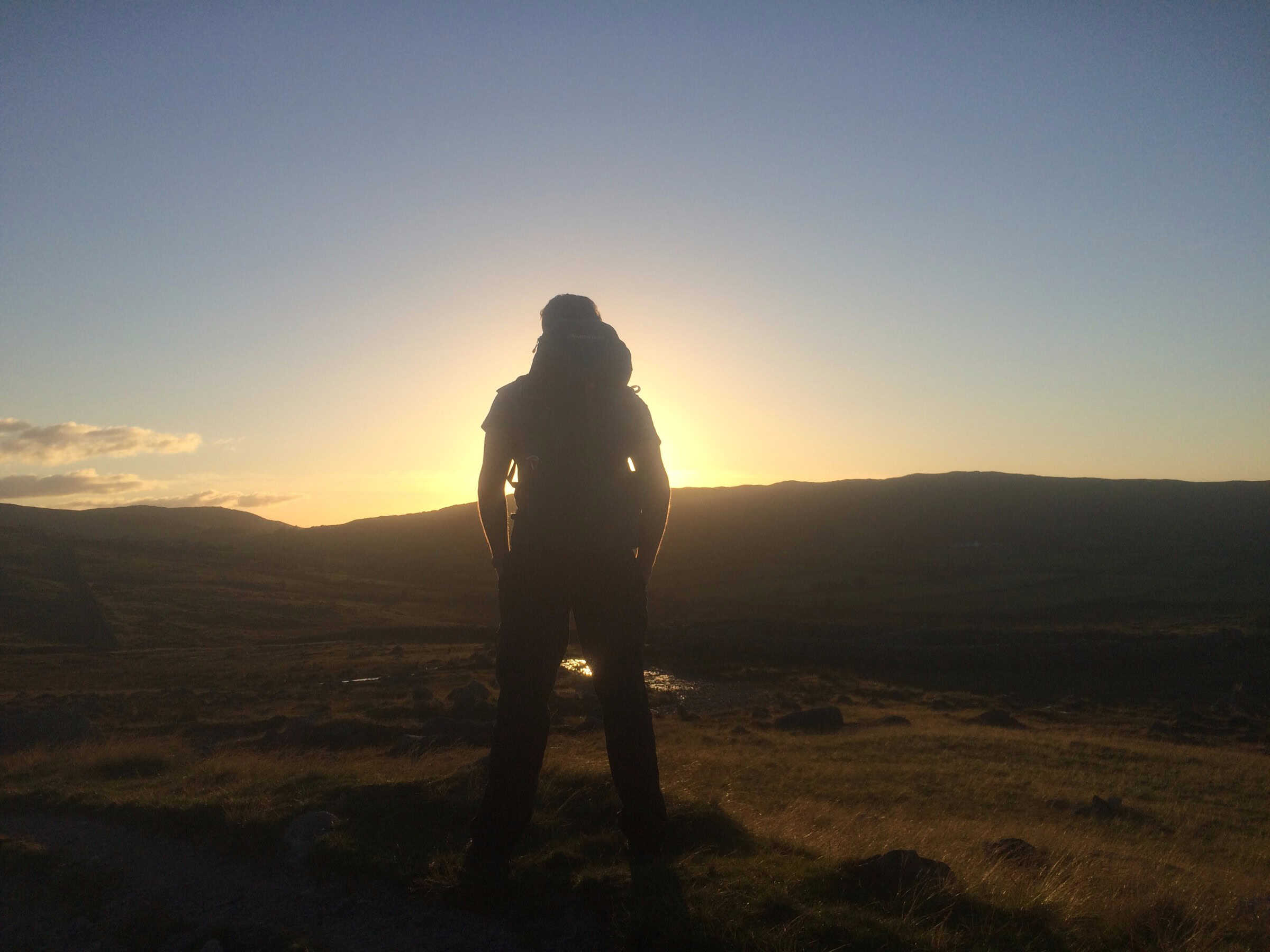 Slievenaglogh Summit Bivi – Monday Microadventure Breathtaking sunset view of hiker silhouette in open countryside, highlighting outdoor adventure and trail exploration.
