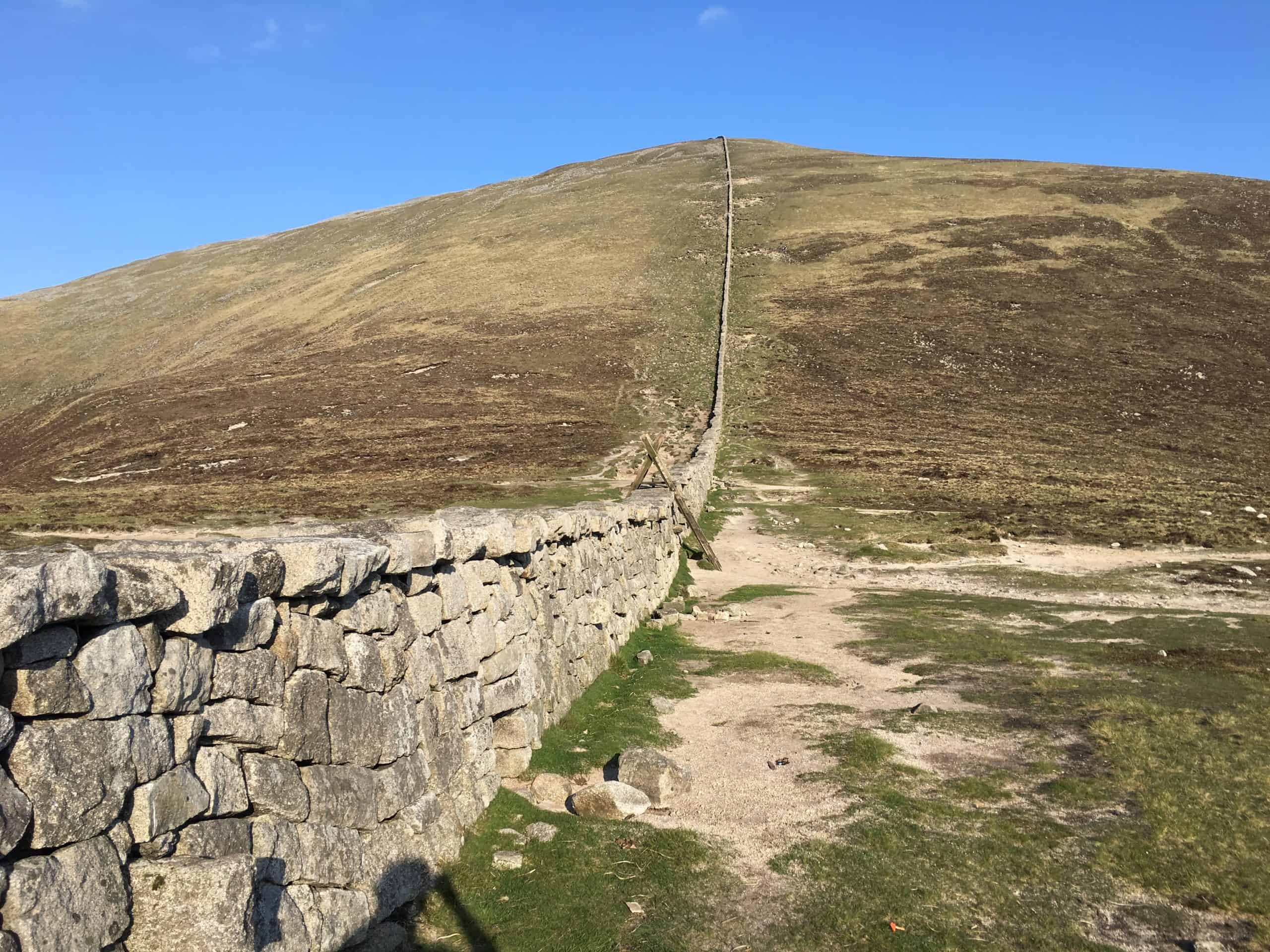Bearnagh via the saddle Rough stone wall on a mountain trail in a rugged outdoor landscape during daytime with clear blue sky.