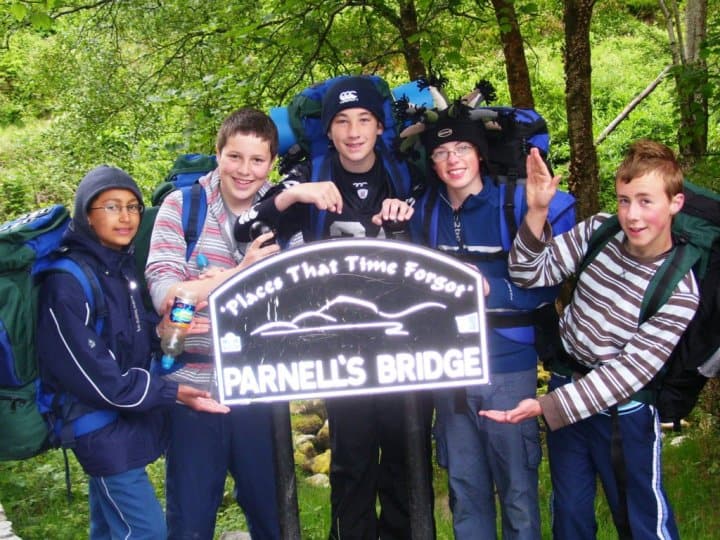 What my Duke of Edinburgh expedition taught me Hikers with backpacks standing in a forest holding a sign that says Parnell's Bridge, enjoying outdoor trekking and hiking adventures in nature.