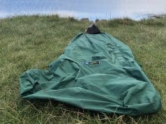 Tips For Bivvy Bag Newbies A green sleeping bag laid out on grassy terrain beside a calm body of water, ideal for outdoor camping and hiking adventures. Perfect for nature lovers seeking tips on wilderness accommodations.