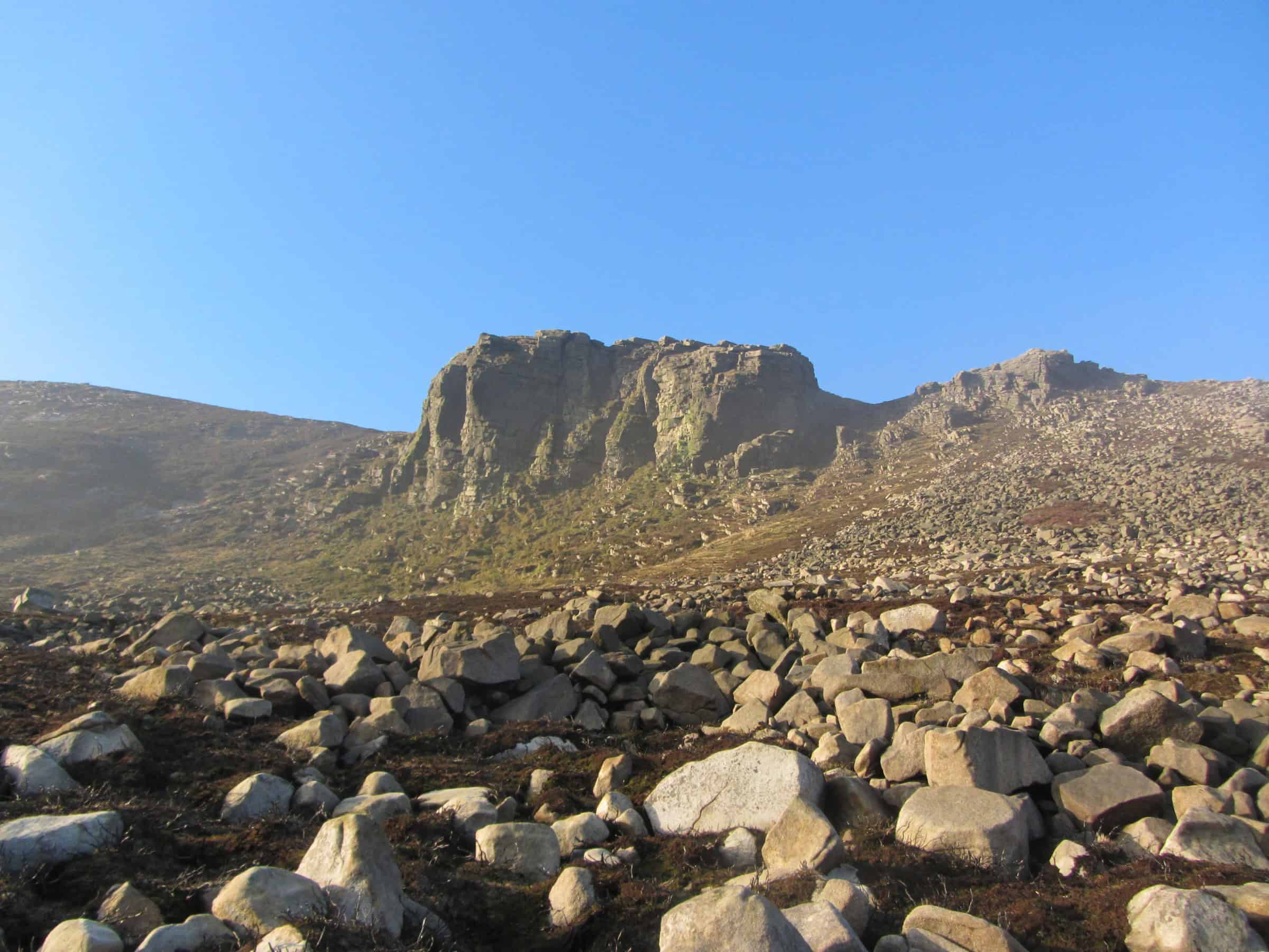 The Land Reader Project Rugged mountain landscape with rocky terrain and steep cliffs under a clear blue sky, ideal for hiking adventures and outdoor exploration.