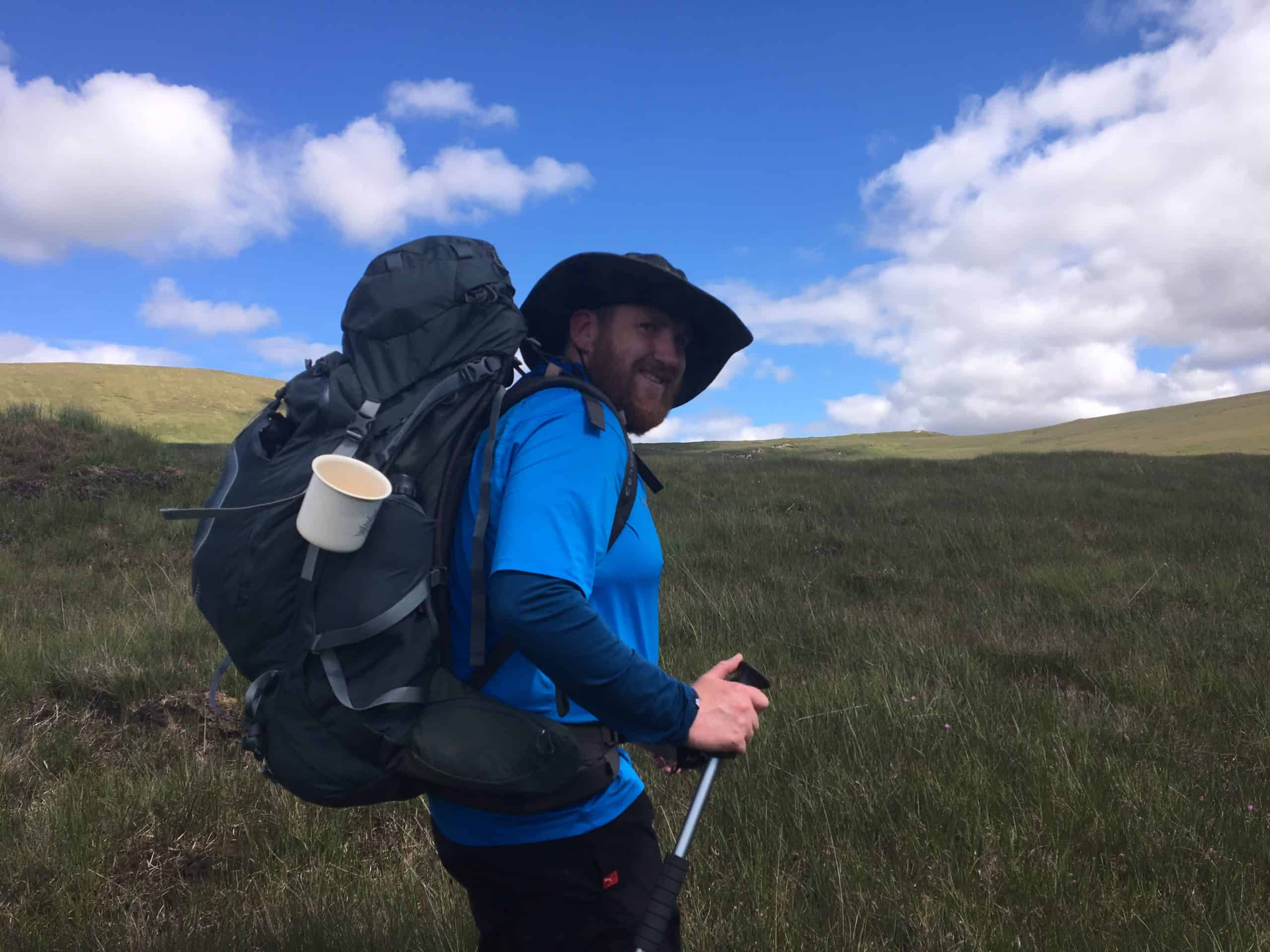 Osprey Xenith 75 Review Hiker with backpack and trekking poles enjoying a scenic outdoor trail in vast grassy hills under a partly cloudy sky.