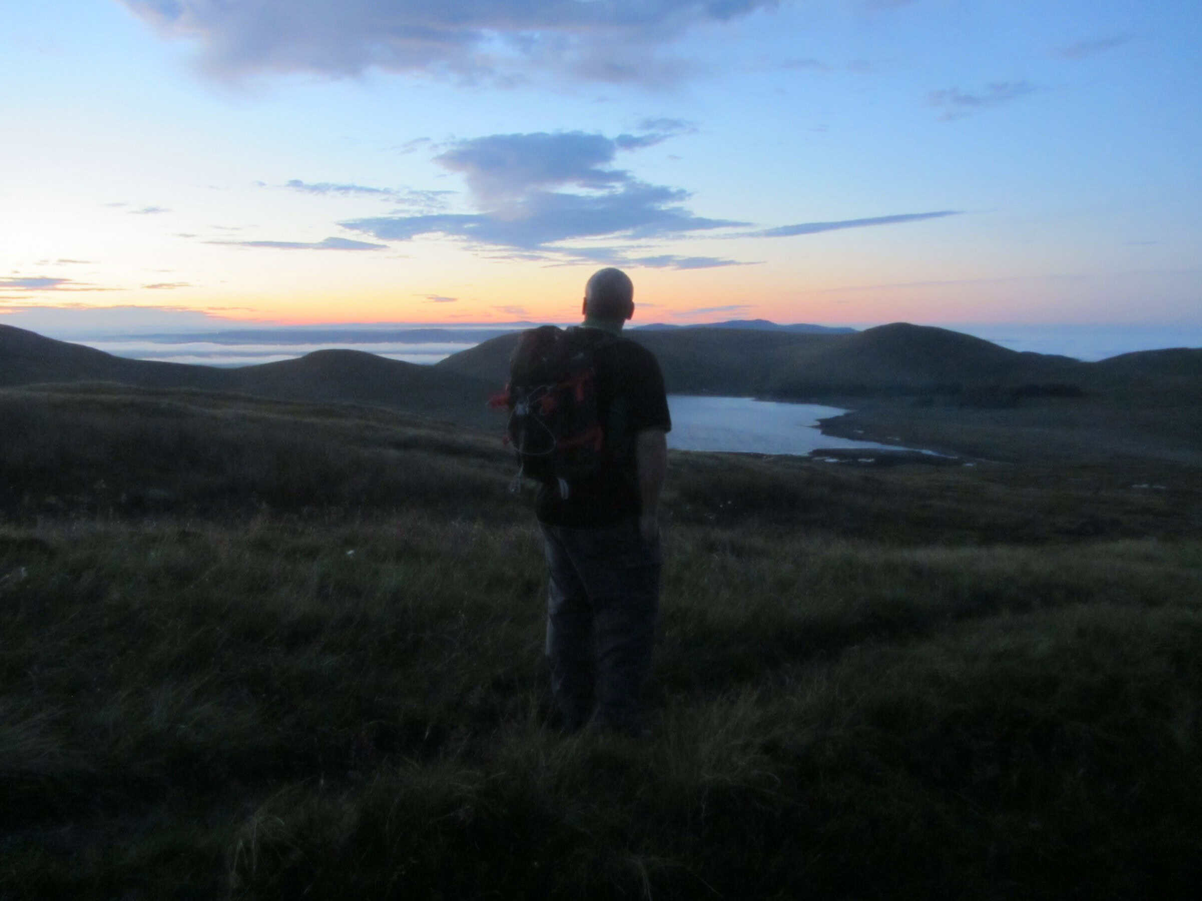 Photo Album: Sunset Ascent of Pigeon Rock Serene hiker overlooking a tranquil lake at sunset in the mountains, capturing outdoor adventure and nature exploration. Beautiful landscape for hiking and trekking enthusiasts.
