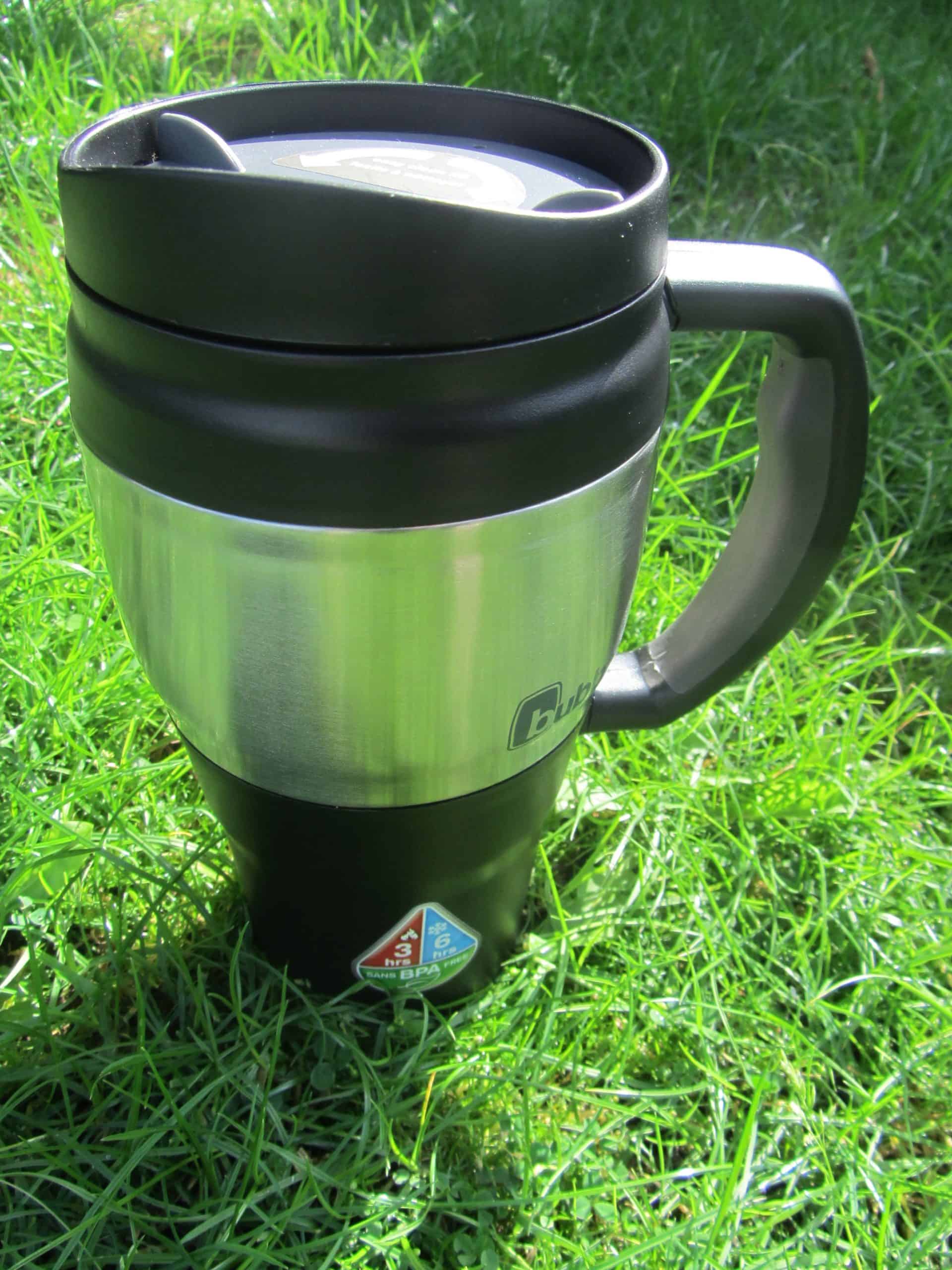 Stainless steel travel mug on green grass, ideal for hiking, outdoor adventures, and camping, featuring BPA-free construction and durable design for hot and cold beverages.