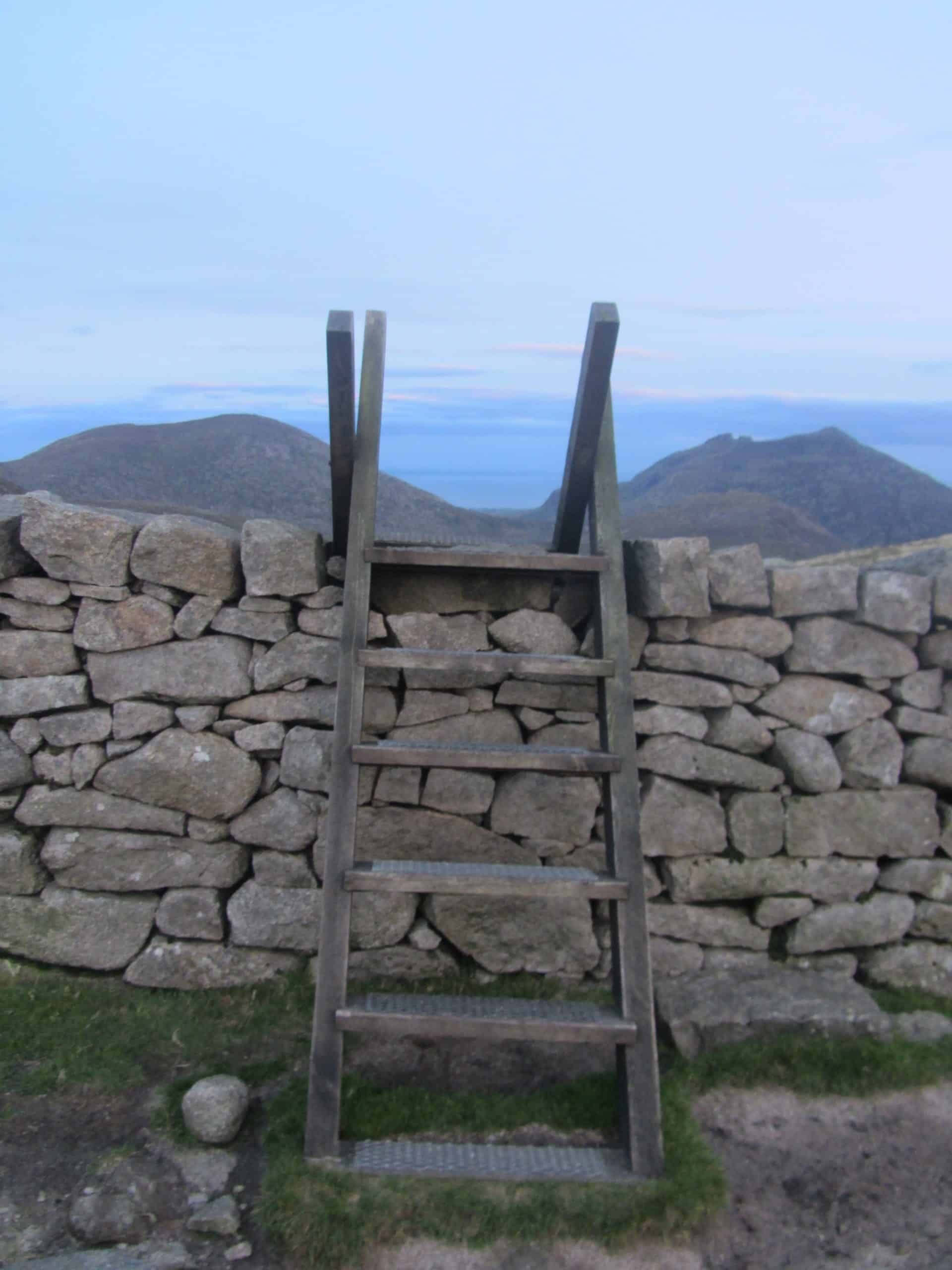 Photo Album: Doan Summit Camp Rustic wooden ladder leaning against a dry stone wall with scenic mountains in the background, perfect for hiking and outdoor adventures around the UK countryside.