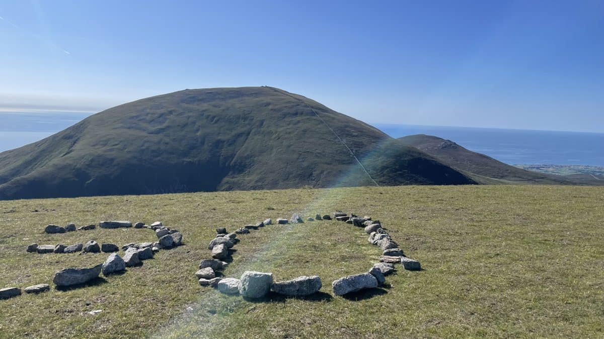 Rocks arranged in a heart shape on mountain summit with rolling hill and sea view, perfect for hiking adventures, outdoor exploration, and scenic trekking on the UK coast.