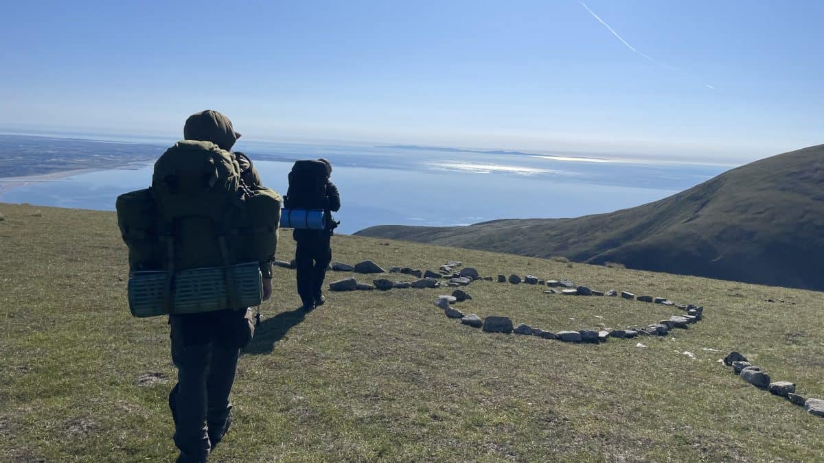 Vibrant hikers exploring scenic mountain trail with a heart-shaped stone formation overlooking a tranquil lake and rolling hills, ideal for outdoor adventure and nature photography.