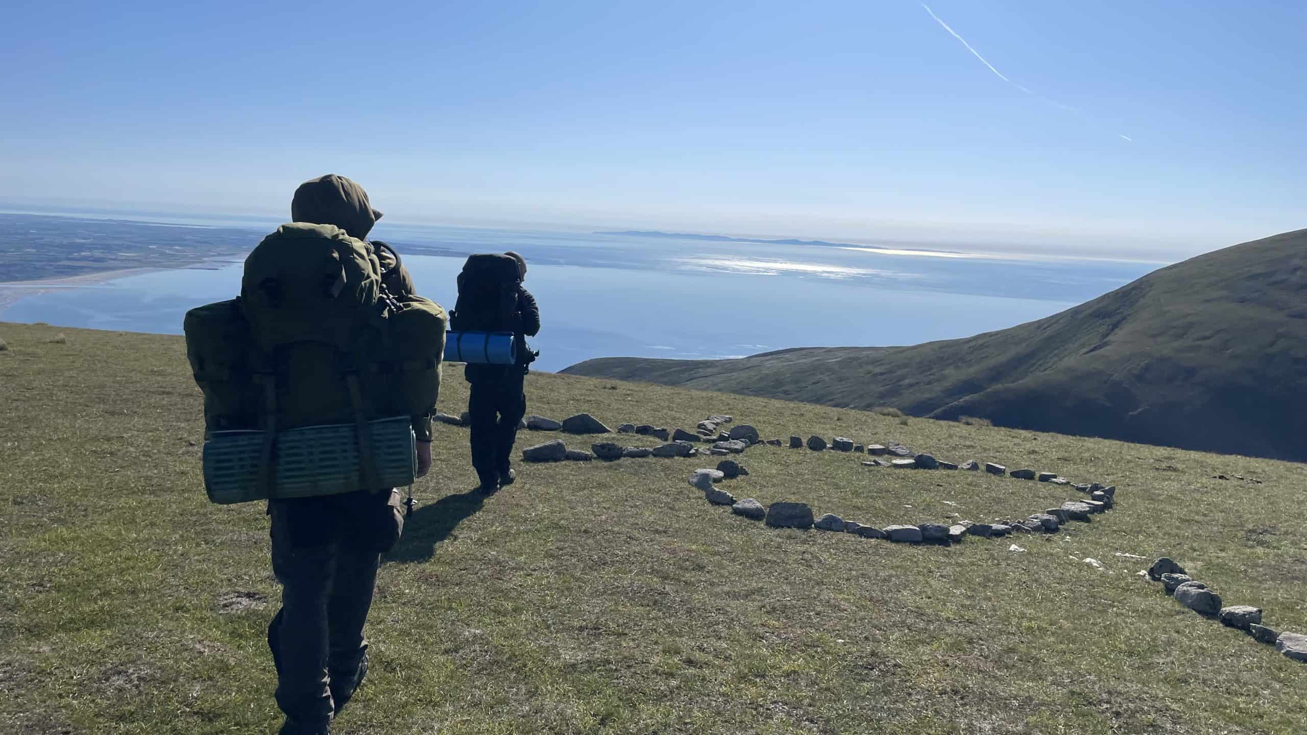 Summer Sunset on Commedagh Summit Vibrant hikers exploring scenic mountain trail with a heart-shaped stone formation overlooking a tranquil lake and rolling hills, ideal for outdoor adventure and nature photography.