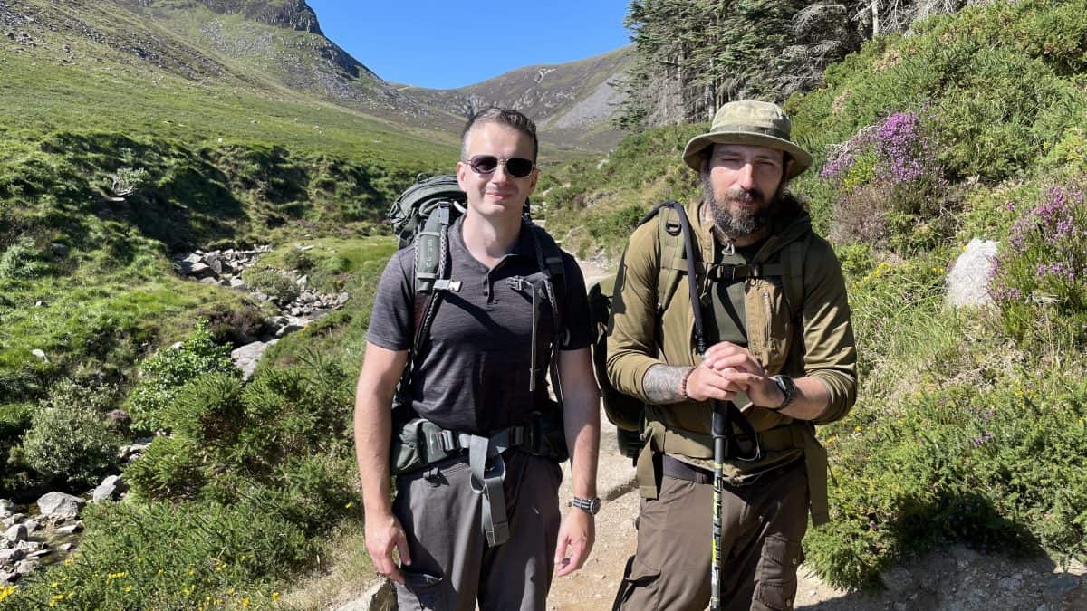 Hiking trail in lush green mountains with two male hikers enjoying outdoor adventure in nature.