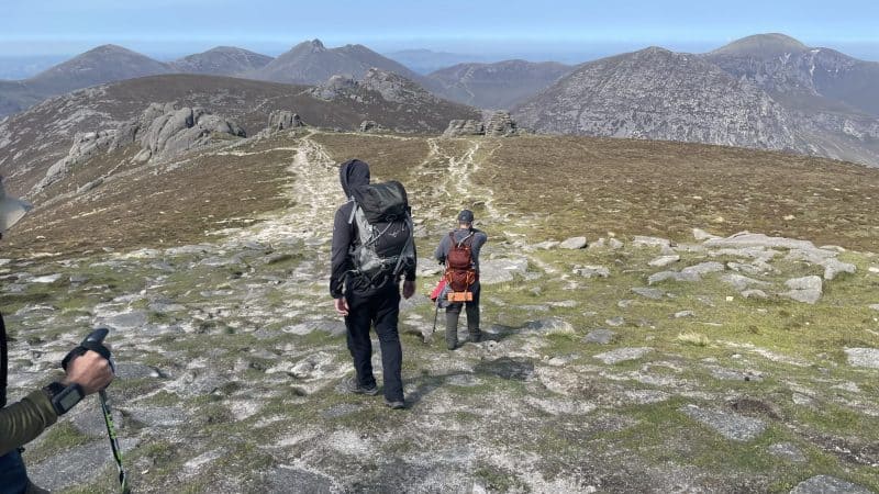 Video: Three Days in the Mournes Hikers walking on a rugged mountain trail with backpacks, surrounded by scenic peaks and clear skies, perfect for outdoor adventure and hiking enthusiasts.