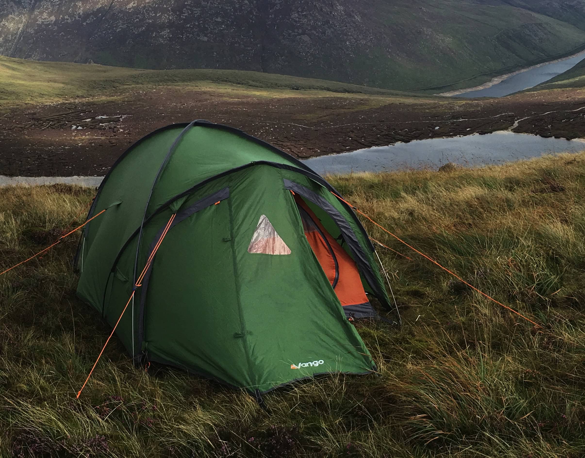 Weekend of Mourne Wild Camping Bright green tent pitched on grassy hillside overlooking a scenic mountain lake in a remote wilderness area. Perfect for outdoor camping, hiking, and exploring nature’s beauty.