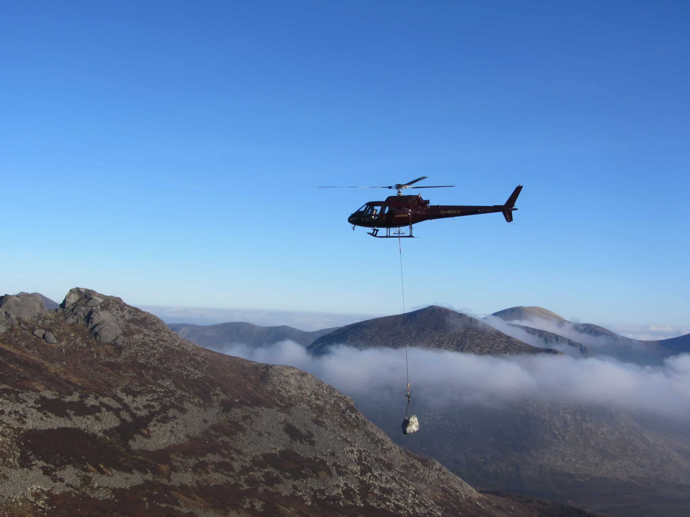 Photo Album: Hot morning on Slieve Binnian Colorful rescue helicopter flying over mountain landscape during daytime.