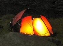 A Mourne Microadventure at the Ben Crom Reservoir Bright orange and red camping tent illuminated at night, set up on grassy terrain for outdoor hiking and camping adventures.